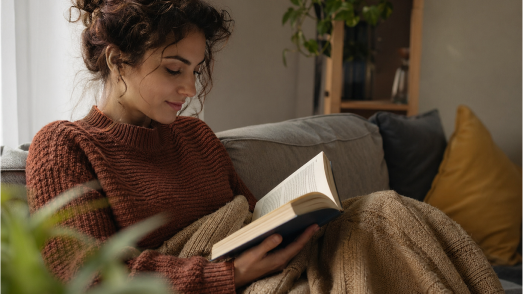Mulher relaxada lendo um livro físico no sofá, praticando o detox digital e recuperando o foco.