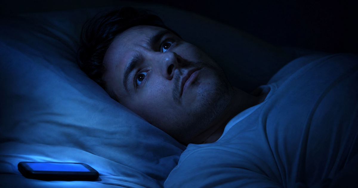 Pessoa com expressão de preocupação e olhos abertos na cama no escuro, ilustrando o sono ansioso e a mente acelerada.